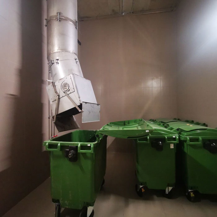 trash chute emptying into green garbage bins