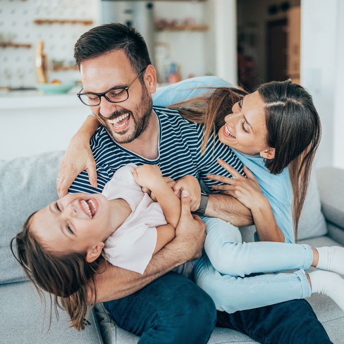 mom and father laughing with young daughter inside home